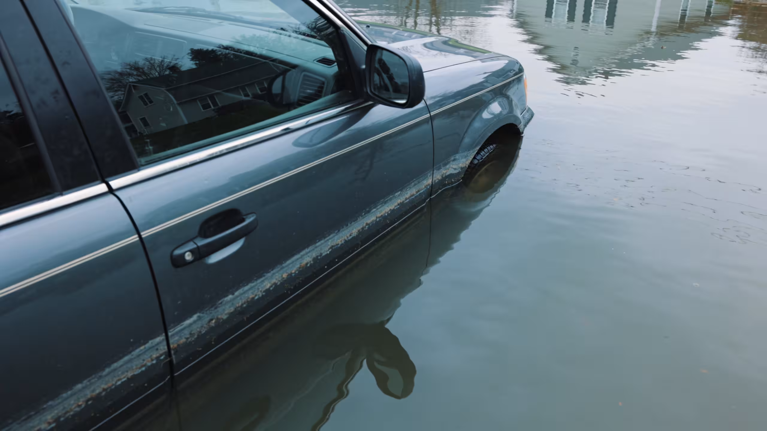 Auto insurance policy documents beside a car in a flooded street after a storm, illustrating does auto insurance cover flood damage