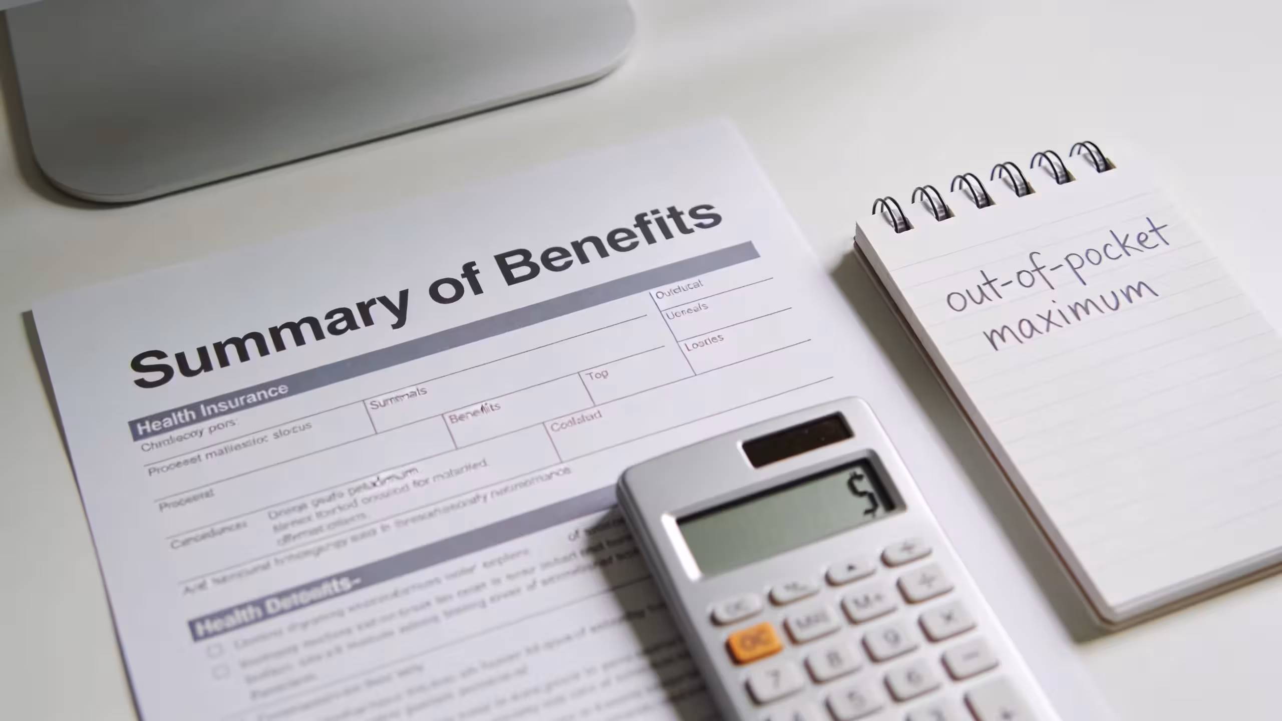 Health insurance documents and calculator on a clean white desk, out-of-pocket maximum