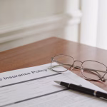 Life insurance for seniors — a wooden desk with an insurance policy document, reading glasses, and a pen in warm indoor lighting