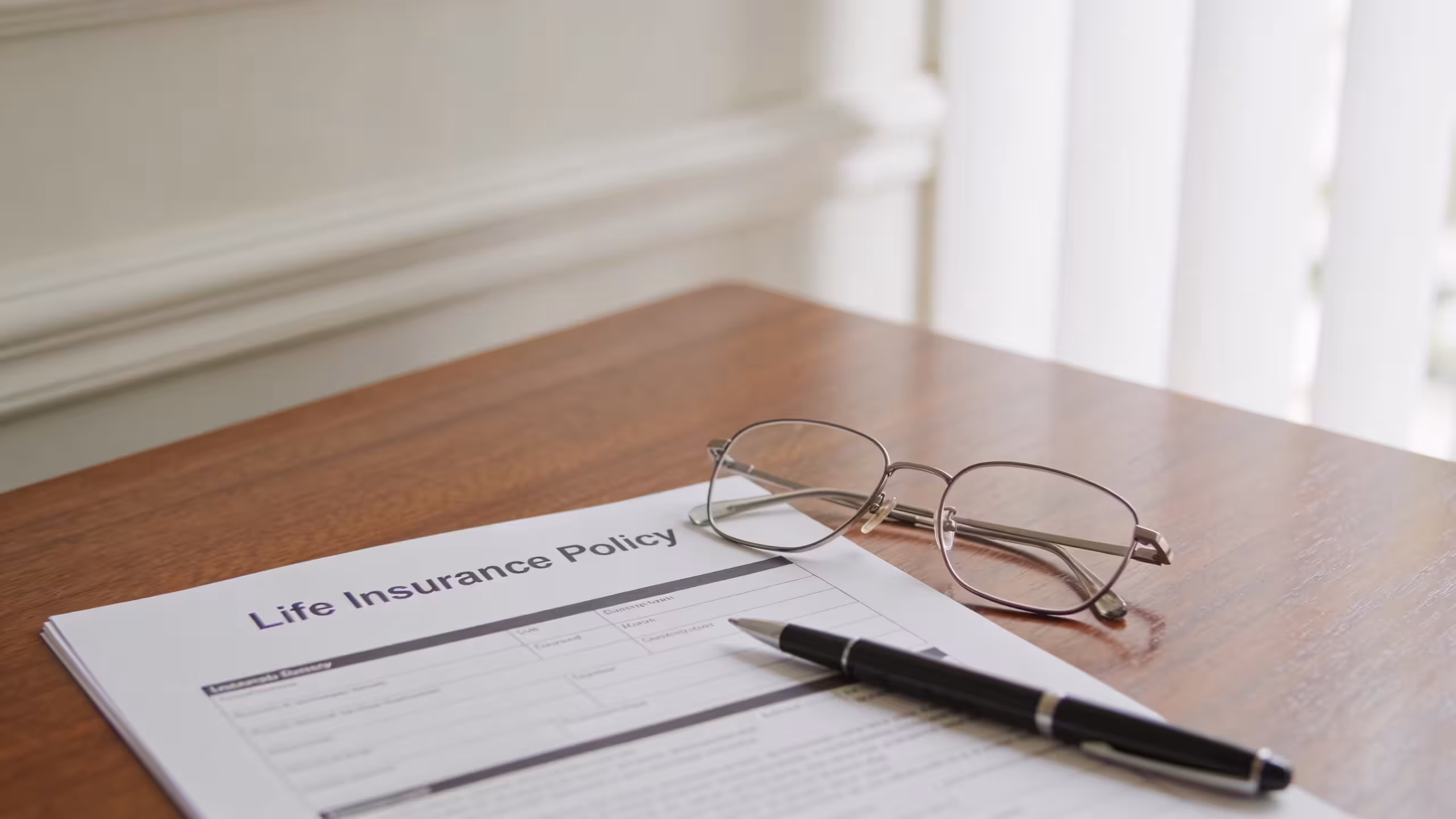 Life insurance for seniors — a wooden desk with an insurance policy document, reading glasses, and a pen in warm indoor lighting